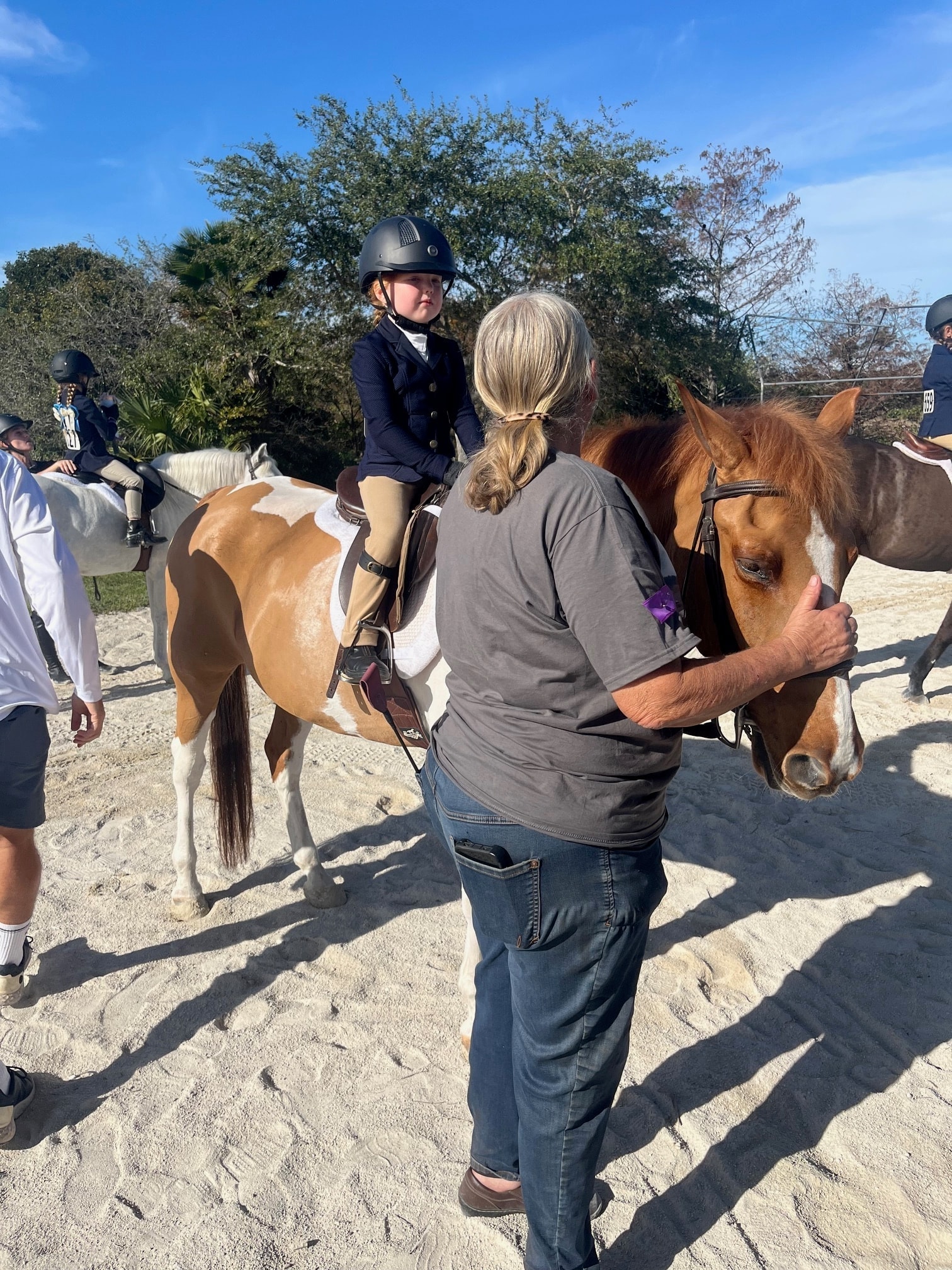 Barb guiding a young rider on a paint horse at a show